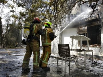 Dos bomberos refrescan el interior de una de las viviendas afectadas por el incendio forestal de Llutxent