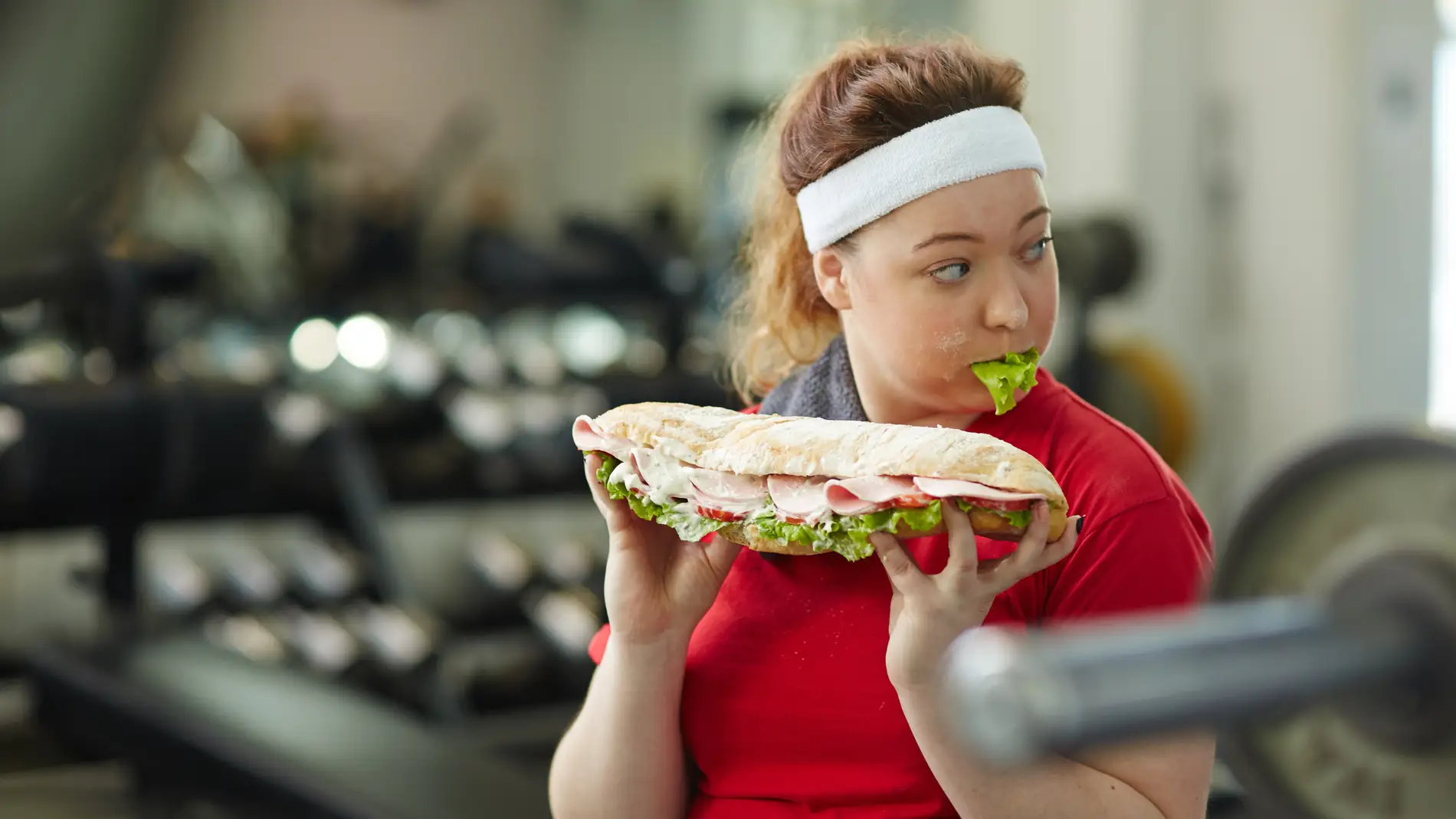 Una chica come un bocadillo enorme en el gimnasio