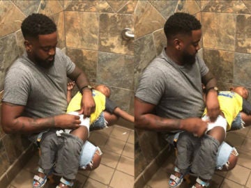 Un padre cambia los pañales de su hijo en un baño sin cambiador