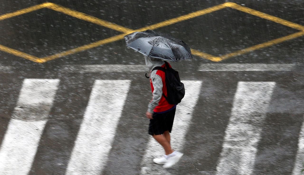 Una persona se protege de la lluvia con un paraguas. Una persona se protege de la lluvia con un paraguas.