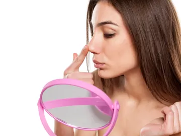 Mujer se mira la nariz frente al espejo Mujer se mira la nariz frente al espejo