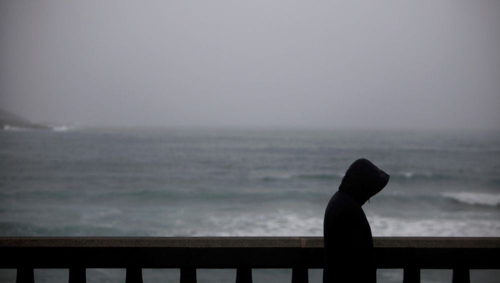 Un hombre camina bajo la lluvia por el paseo marítimo de A Coruña