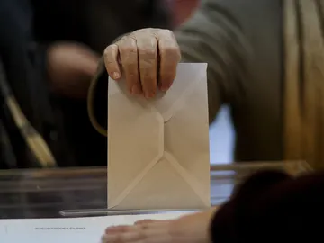 Una persona introduce un sobre en una urna electoral. Una persona introduce un sobre en una urna electoral.