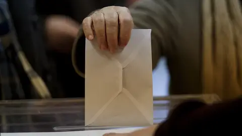 Una persona introduce un sobre en una urna electoral. Una persona introduce un sobre en una urna electoral.