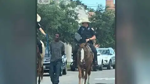 Dos policías llevan maniatado a un hombre negro detenido Dos policías llevan maniatado a un hombre negro detenido