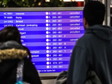 Unos pasajeros mirando los vuelos cancelados en la pantalla informativa Unos pasajeros mirando los vuelos cancelados en la pantalla informativa