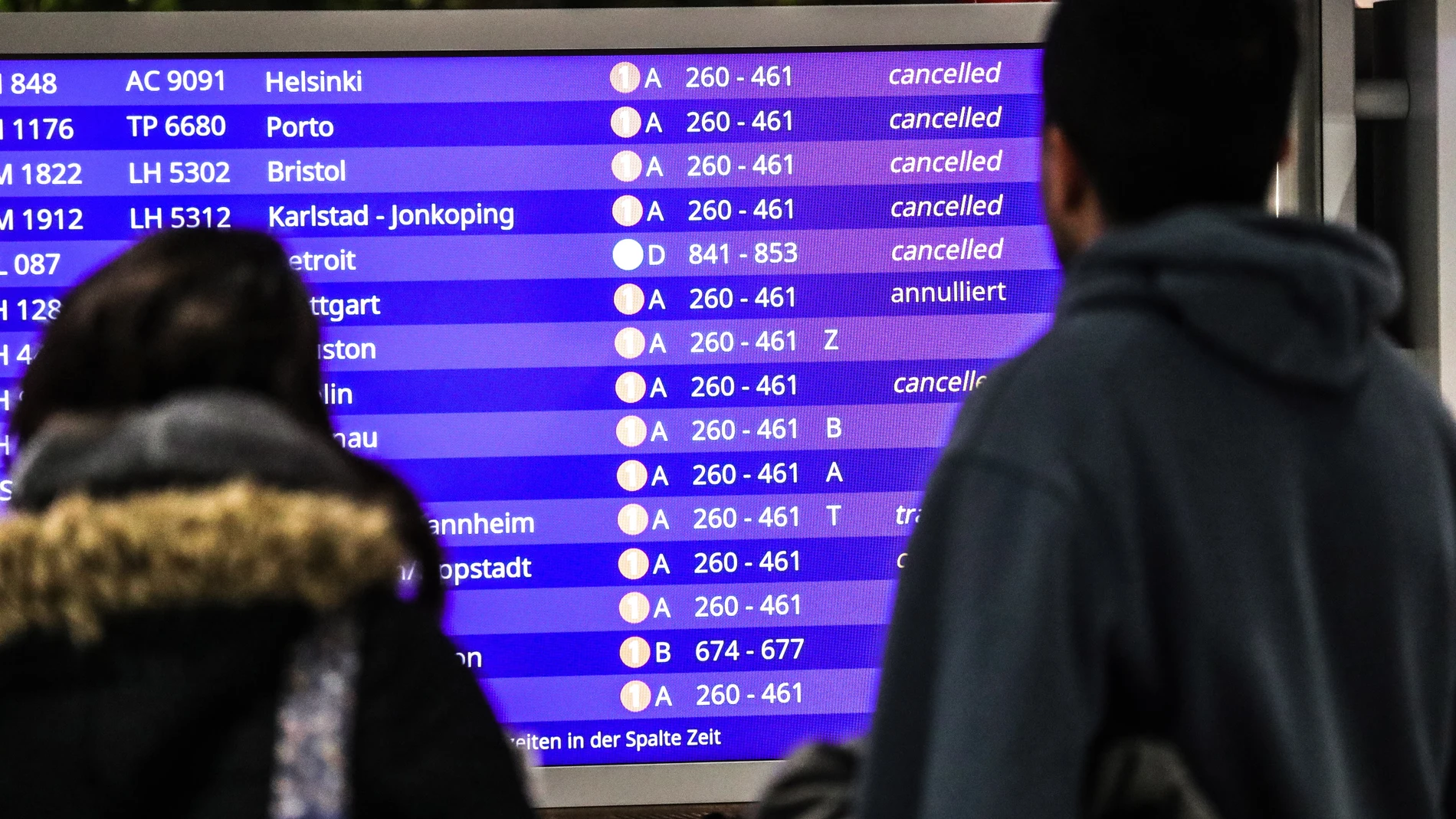 Unos pasajeros mirando los vuelos cancelados en la pantalla informativa Unos pasajeros mirando los vuelos cancelados en la pantalla informativa