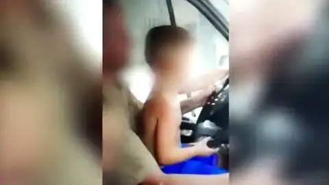 Graban a un niño al volante de un coche sentado en las rodillas de su padre Graban a un niño al volante de un coche sentado en las rodillas de su padre
