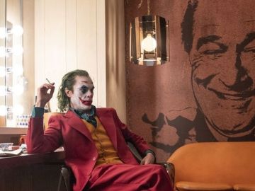 Joker (Joaquin Phoenix) con una imagen al fondo de Murray Franklin (Robert De Niro)