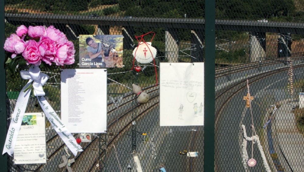 Diversos objetos en recuerdo y homenaje de las víctimas cuelgan de la valla en el paso elevado sobre la curva de A Grandeira