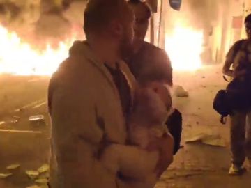  Un hombre sale con su bebé en brazos huyendo de las llamas que amenazan su casa por las protestas en Barcelona