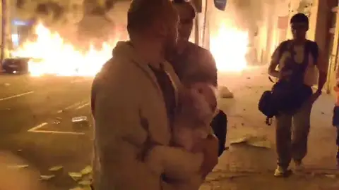 Un hombre sale con su bebé en brazos huyendo de las llamas que amenazan su casa por las protestas en Barcelona Un hombre sale con su bebé en brazos huyendo de las llamas que amenazan su casa por las protestas en Barcelona