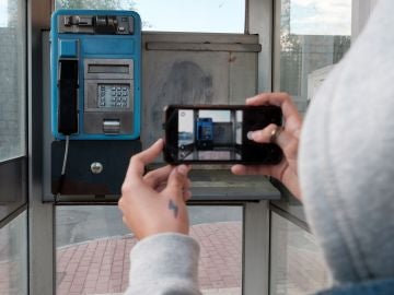 Una joven toma con su teléfono móvil una fotografía de una cabina telefónica en un barrio de Ávila