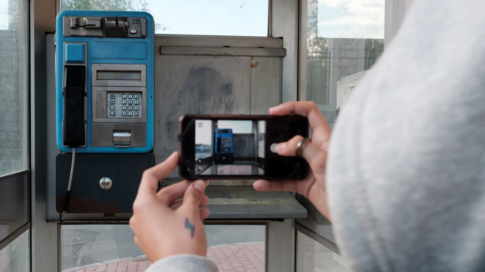 Una joven toma con su teléfono móvil una fotografía de una cabina telefónica en un barrio de Ávila Una joven toma con su teléfono móvil una fotografía de una cabina telefónica en un barrio de Ávila