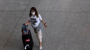 Una mujer con una mascarilla desplaz&aacute;ndose con una maleta