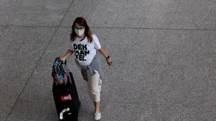 Una mujer con una mascarilla desplazándose con una maleta Una mujer con una mascarilla desplazándose con una maleta