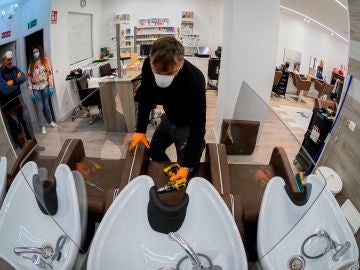 Imagen tomada con una lente ojo de pez de un obrero mientras instala mamparas de separación entre las pilas para lavar cabezas en una peluquería de Alcalá de Henares, Madrid