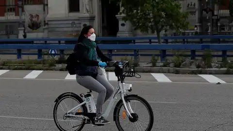 Una mujer con mascarilla y guantes usa una bici de biciMad en Madrid Una mujer con mascarilla y guantes usa una bici de biciMad en Madrid