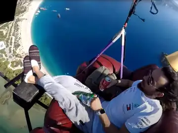 Un hombre vuela en parapente sentado tranquilamente en un sofá mientra se toma un aperitivo Un hombre vuela en parapente sentado tranquilamente en un sofá mientra se toma un aperitivo
