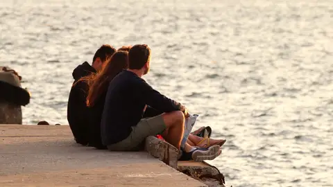 Un grupo de jóvenes charla al atardecer en una playa Un grupo de jóvenes charla al atardecer en una playa