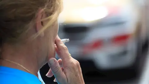 Una mujer se fuma un cigarrillo Una mujer se fuma un cigarrillo