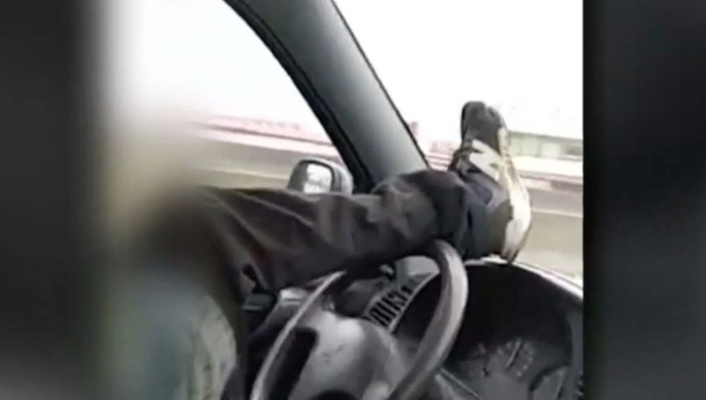 Dos jóvenes se graban conduciendo en dirección contraria y manejando el volante con el pie por una carrtera de Astillero