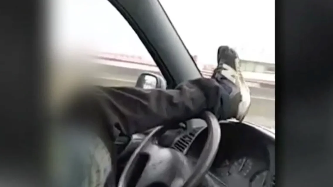 Dos jóvenes se graban conduciendo en dirección contraria y manejando el volante con el pie por una carrtera de Astillero Dos jóvenes se graban conduciendo en dirección contraria y manejando el volante con el pie por una carrtera de Astillero
