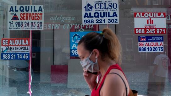 Una mujer con mascarilla pasa ante un comercio cerrado con varios carteles que anuncian su alquiler