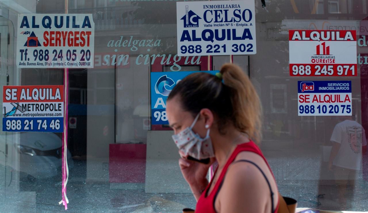 Una mujer con mascarilla pasa ante un comercio cerrado con varios carteles que anuncian su alquiler