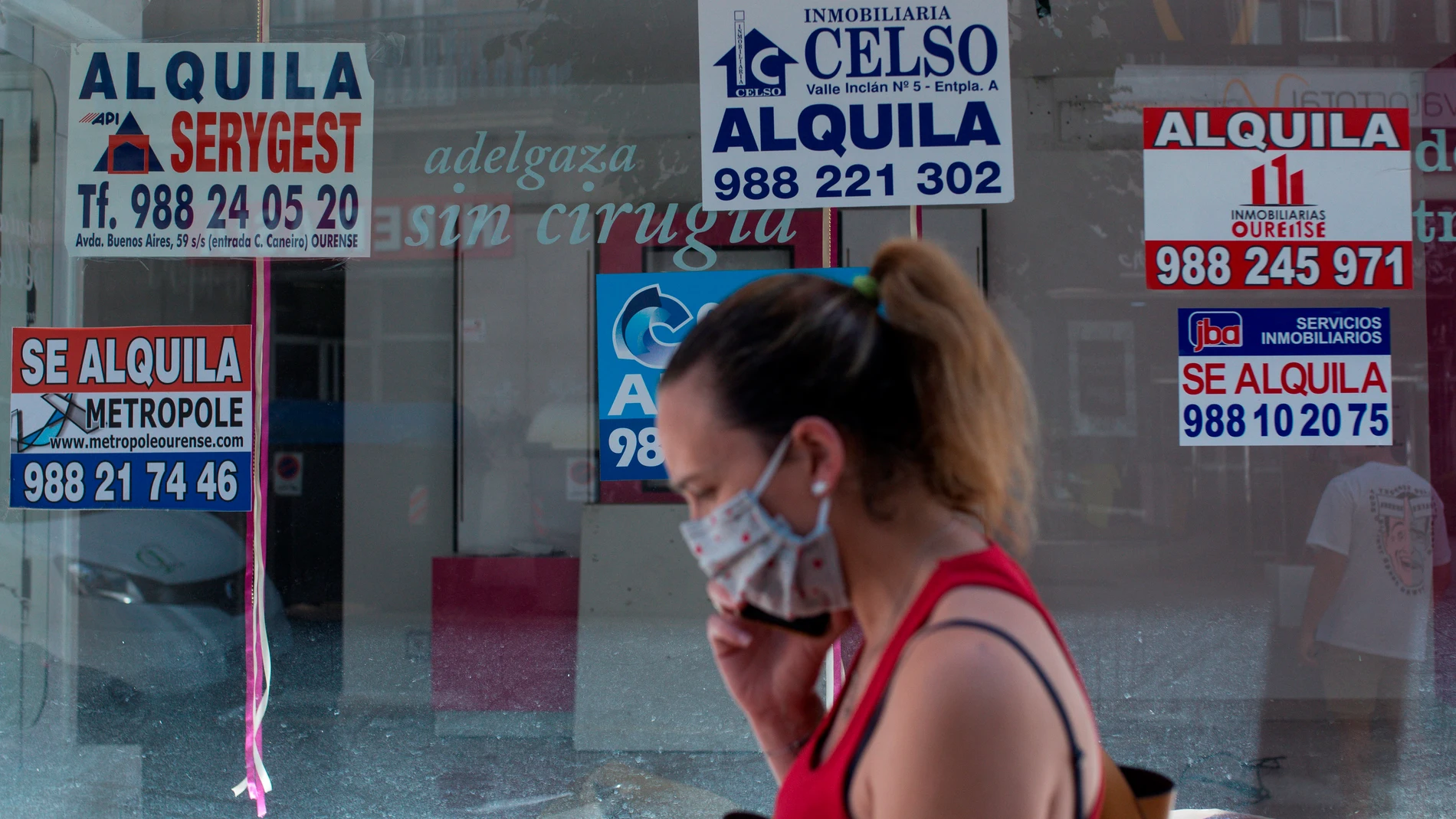 Una mujer con mascarilla pasa ante un comercio cerrado con varios carteles que anuncian su alquiler Una mujer con mascarilla pasa ante un comercio cerrado con varios carteles que anuncian su alquiler