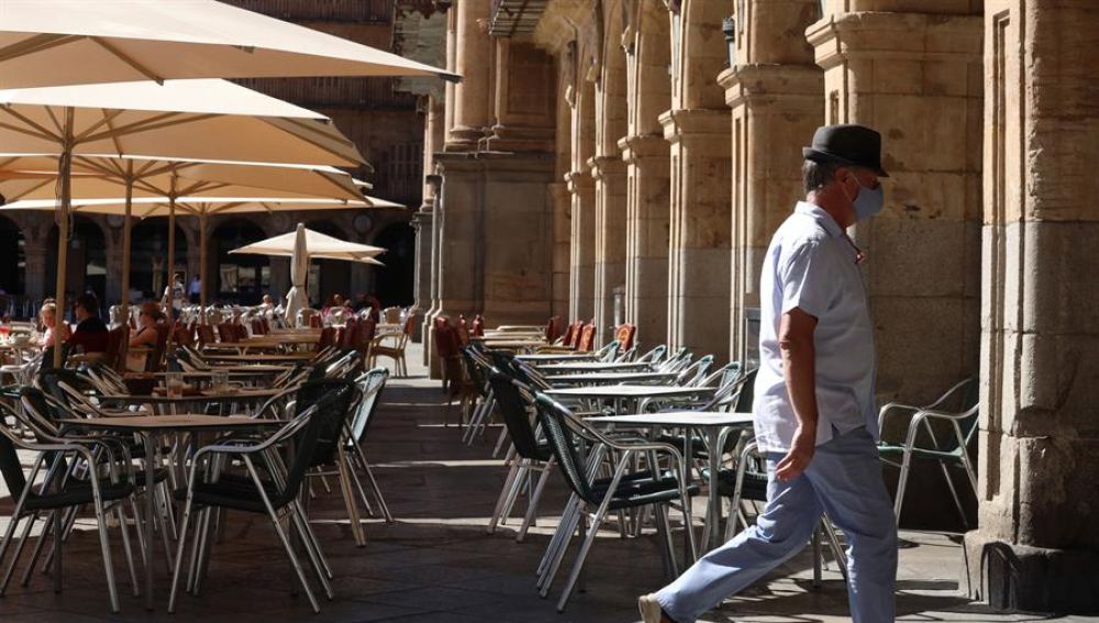 Un hombre con mascarilla pasa frente a una terraza de un restaurante de la plaza mayor de Salamanca.