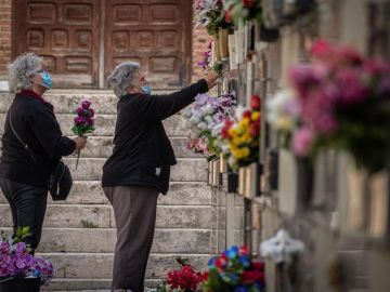 Varias mujeres colocan flores en una tumba del cementerio de Alcalá