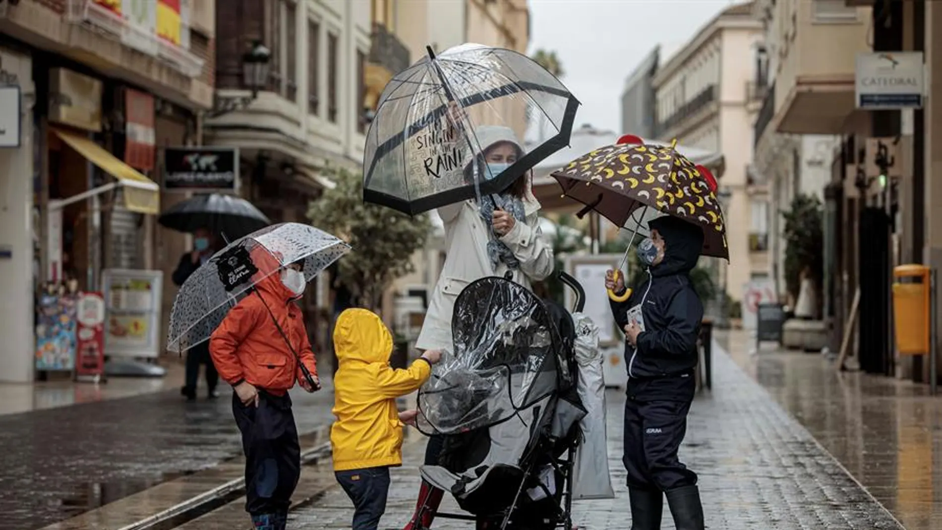 Una mujer con tres menores se protegen de la lluvia con paraguas y chubasqueros Una mujer con tres menores se protegen de la lluvia con paraguas y chubasqueros