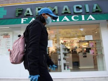 Una viandante, protegida con guantes y mascarilla, pasa por delante de una farmacia.