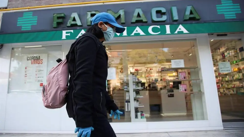 Una viandante, protegida con guantes y mascarilla, pasa por delante de una farmacia. Una viandante, protegida con guantes y mascarilla, pasa por delante de una farmacia.
