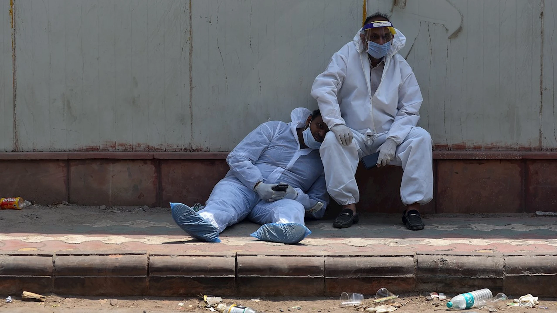 Dos paramédicos indios se toman un descanso a las puertas del depósito de cadáveres de un hospital en Nueva Delhi (India) este jueves