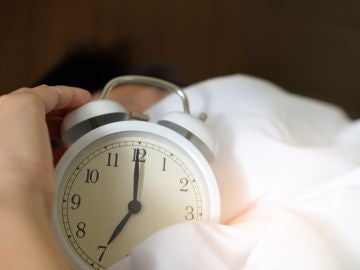 Una persona sujetando un reloj despertador mientras duerme