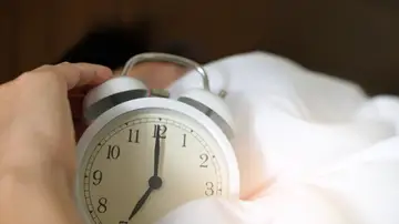 Una persona sujetando un reloj despertador mientras duerme