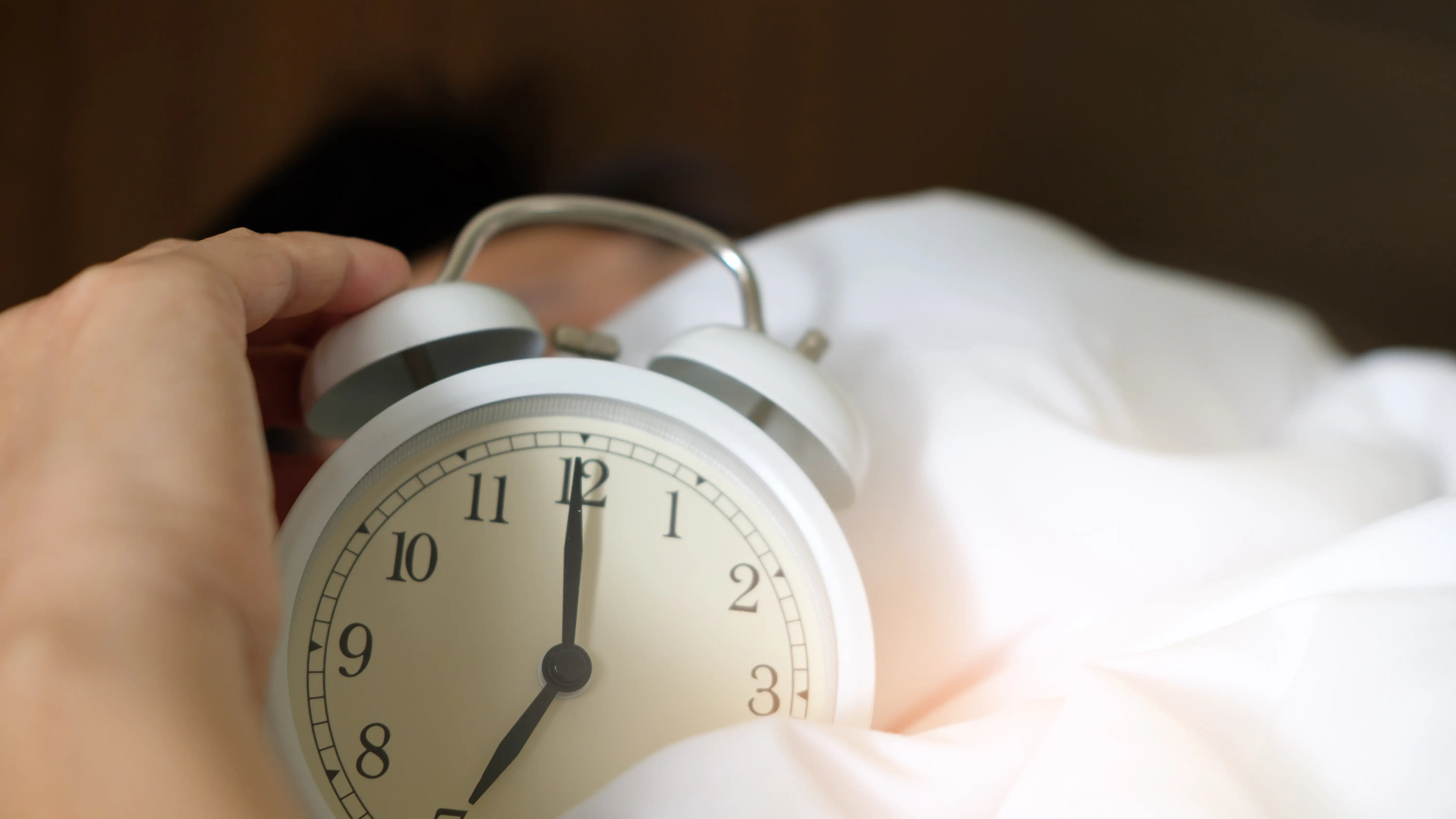Una persona sujetando un reloj despertador mientras duerme Una persona sujetando un reloj despertador mientras duerme