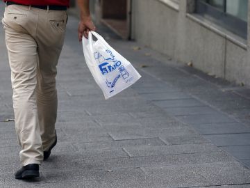 Un hombre camina por la calle portando una bolsa de plástico