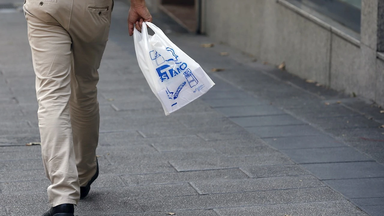 Un hombre camina por la calle portando una bolsa de plástico Un hombre camina por la calle portando una bolsa de plástico