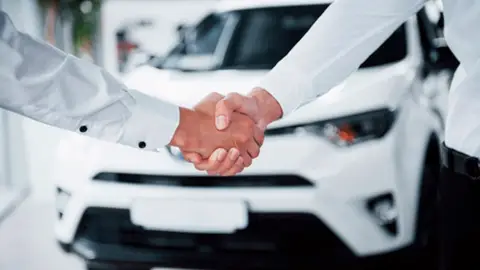 Dos hombres se estrechan las manos ante un coche de renting Dos hombres se estrechan las manos ante un coche de renting