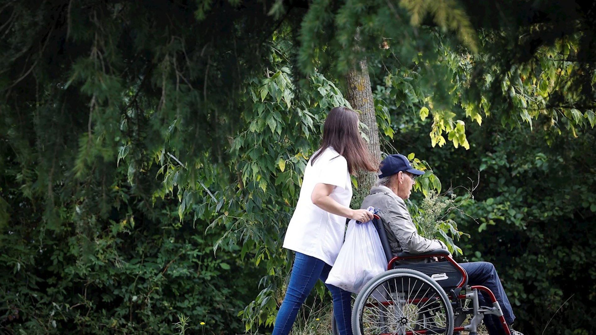 Una trabajadora de una residencia pasea a un anciano en silla de ruedas
