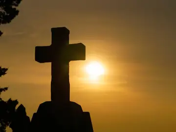 Imagen de una cruz con el sol de fondo