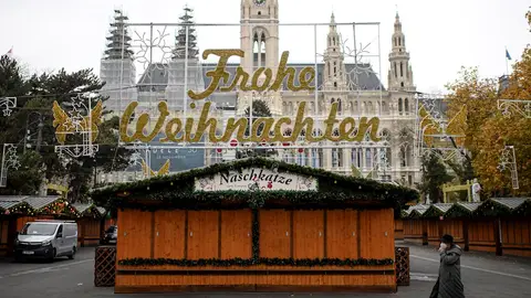 Una mujer camina por un mercado navideño cerrado frente al ayuntamiento de Viena. Una mujer camina por un mercado navideño cerrado frente al ayuntamiento de Viena.