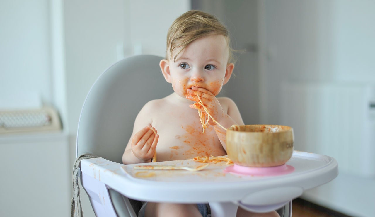 Bebé comiendo un plato de espaguetis con las manos. 