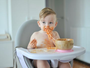 Bebé comiendo un plato de espaguetis con las manos. 