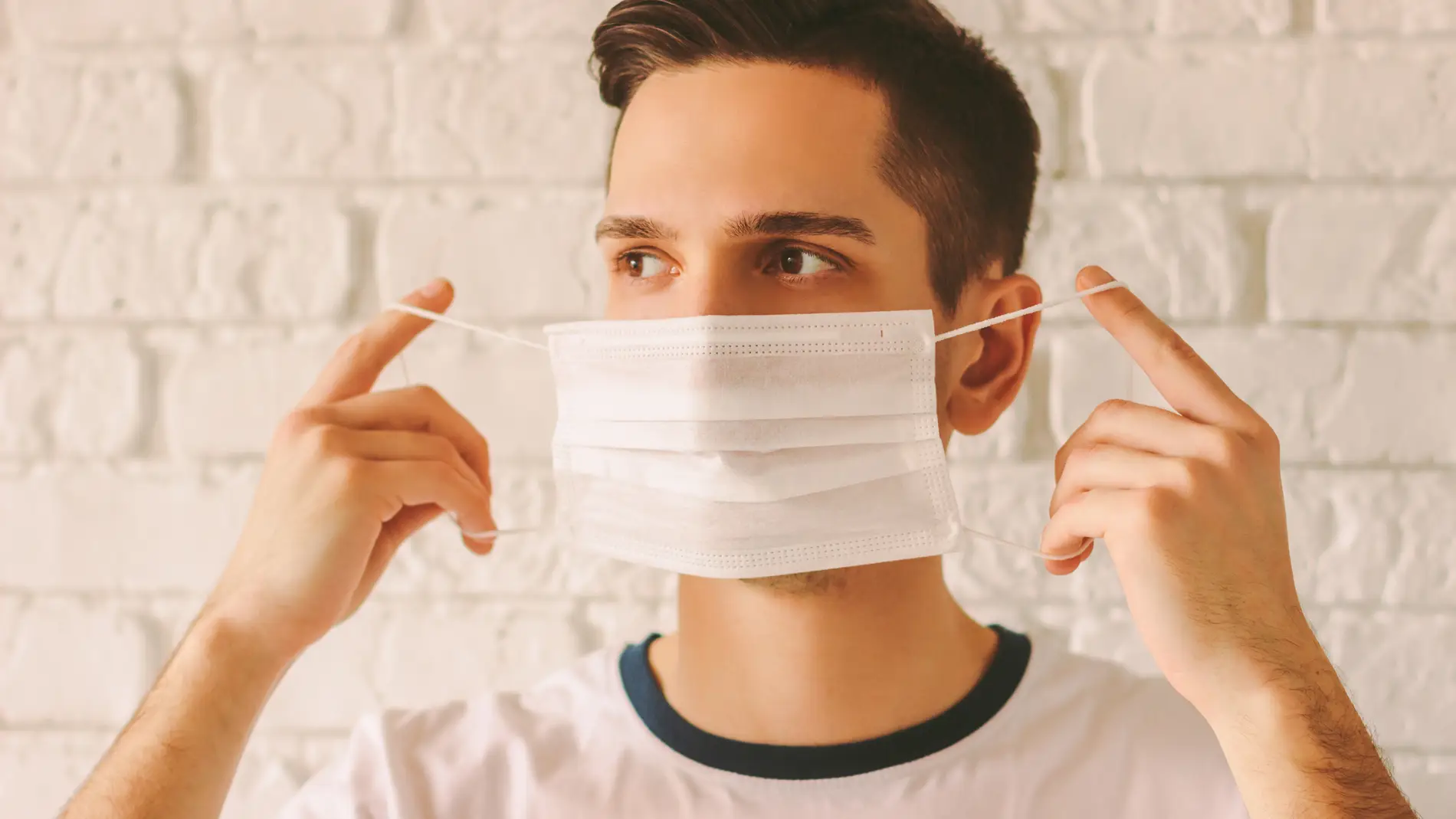 Un chico se pone la mascarilla quirúrgica.