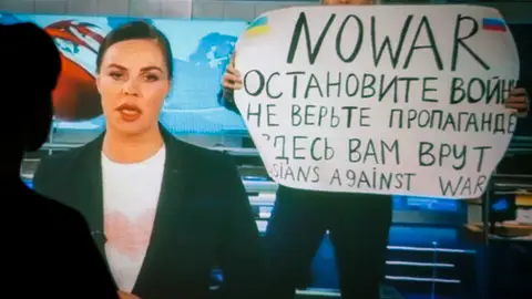 Una mujer ve una transmisión grabada del programa de televisión de noticias del canal ruso Channel One en el que un empleado entró en el estudio con un cartel que se podía leer "No a la guerra". Detengan la guerra. No creas en la propaganda. Aquí te están mintiendo Una mujer ve una transmisión grabada del programa de televisión de noticias del canal ruso Channel One en el que un empleado entró en el estudio con un cartel que se podía leer "No a la guerra". Detengan la guerra. No creas en la propaganda. Aquí te están mintiendo