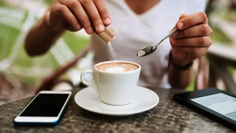Mujer añadiendo azúcar a su café Mujer añadiendo azúcar a su café